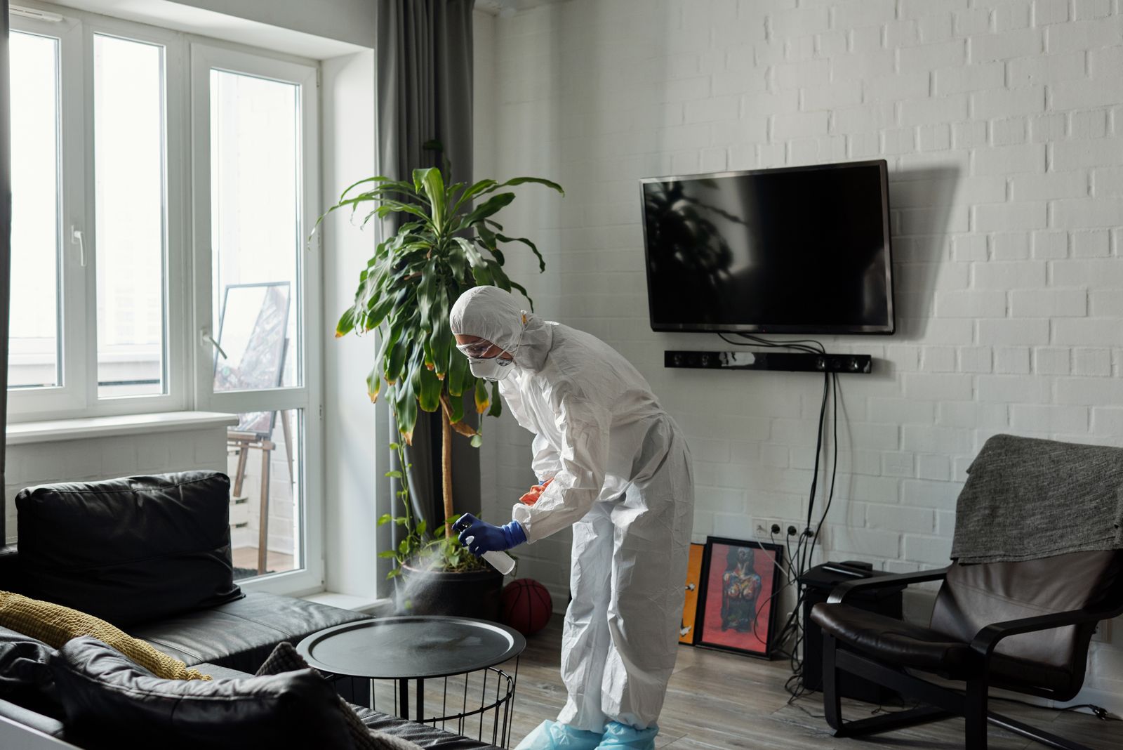 A worker in protective gear disinfecting a surface with a spray bottle